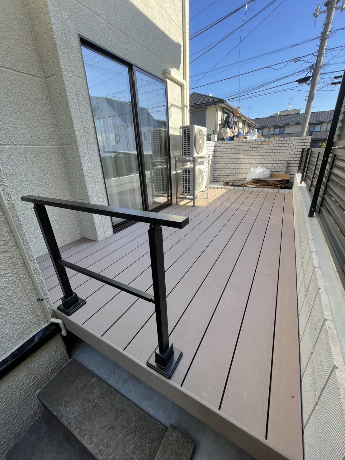 住宅側面の細長いスペースに施工したウッドデッキと黒いアルミ手すり、コンクリートの階段